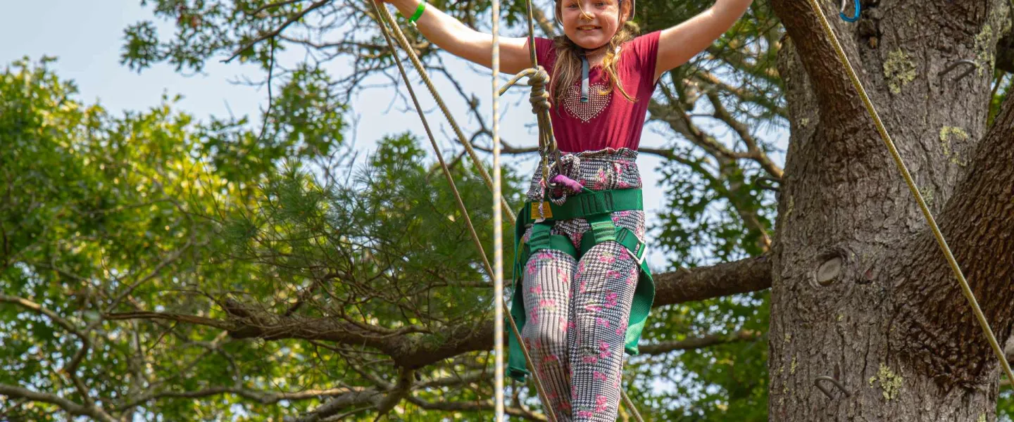 Smiling girl wearing a helmet walking the ropes at Camp Clarks ropes course