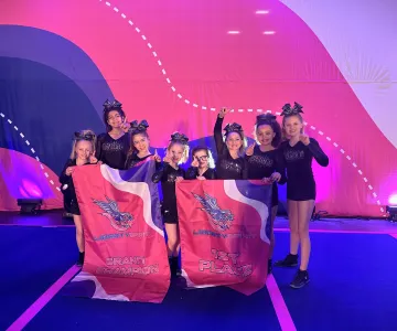 8 cheerleaders holding up their 1st place flag for the Liberty Spirit Grand Champion in excitement