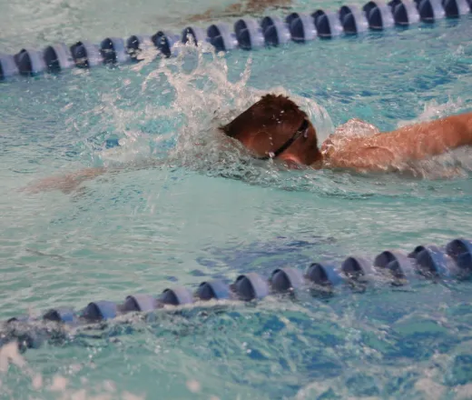 Young kid with goggles swimming at a swim meet in a pool